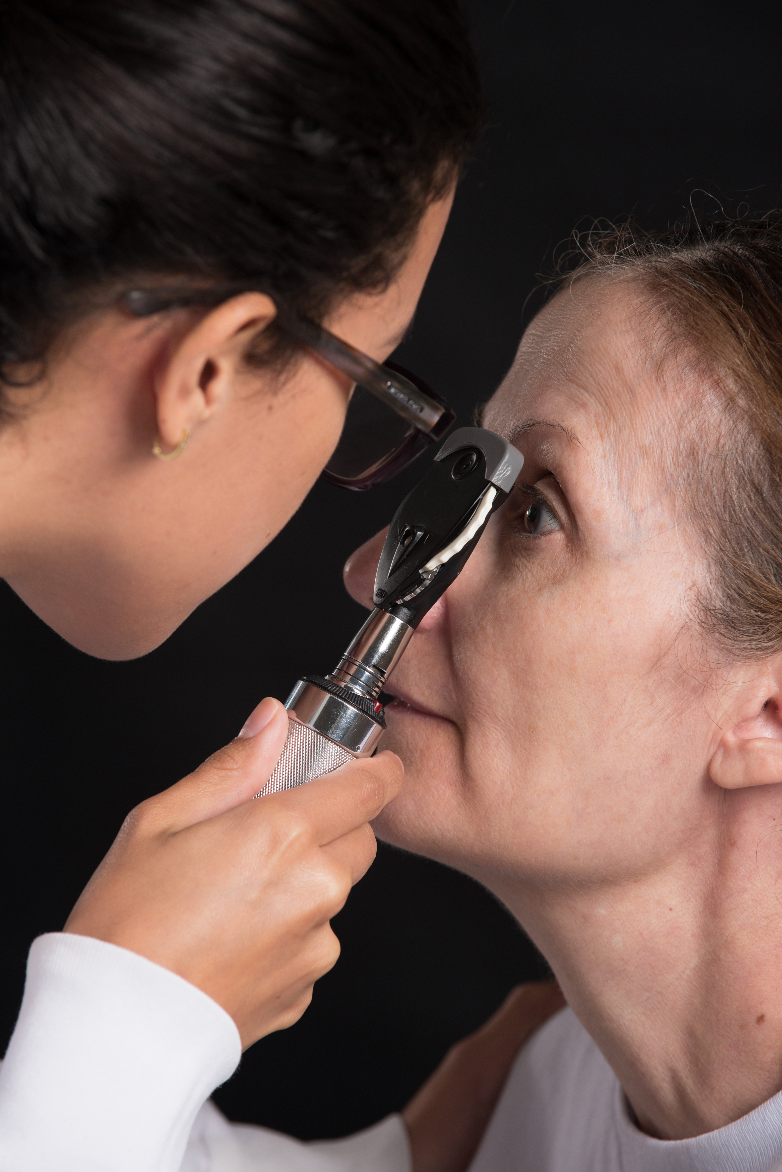 A doctor using an ophthalmoscope to check a patient's left eye.