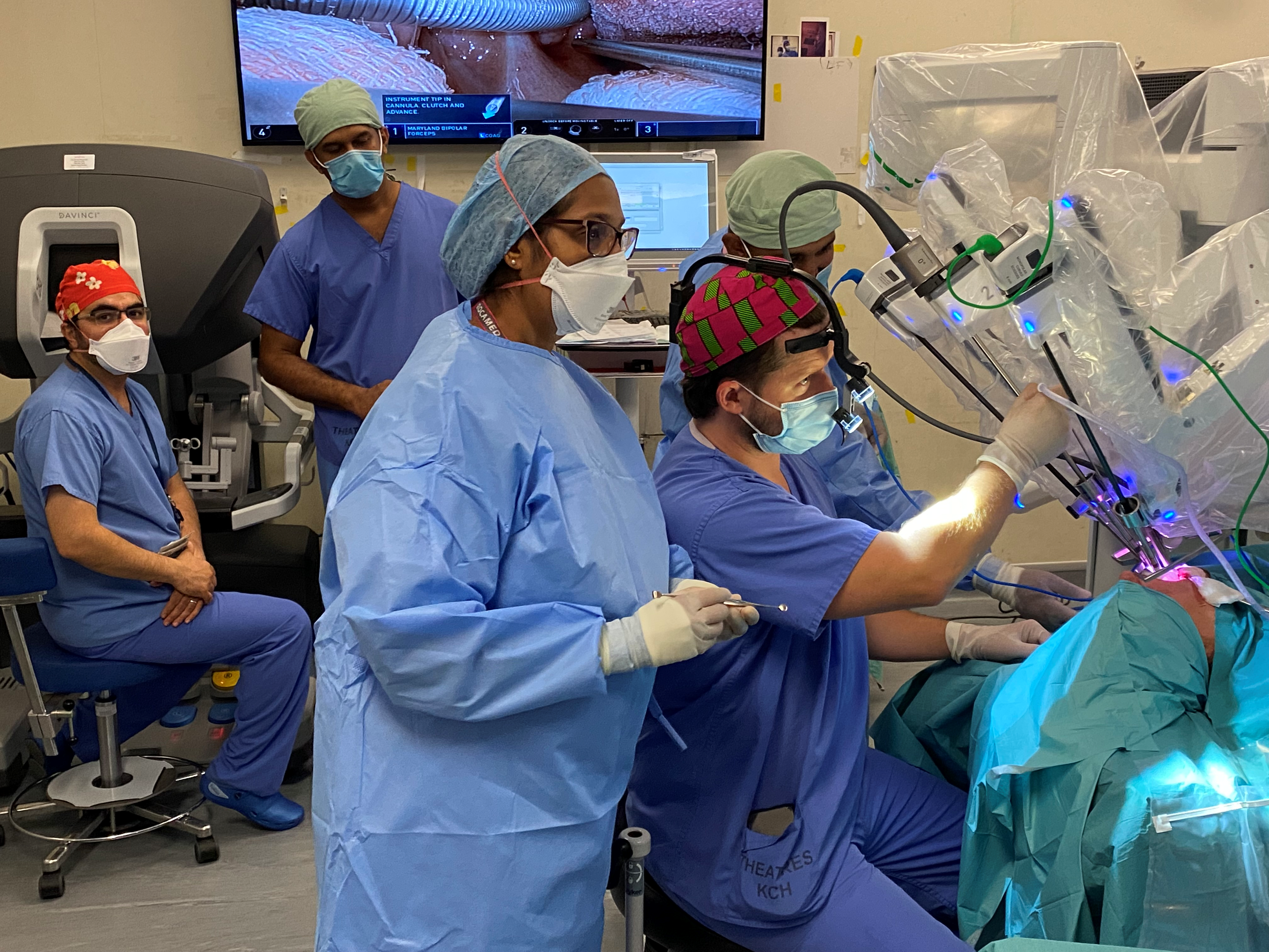 Medical staff with blue scrubs and masks on, performing trans oral surgery using a machine (robot).